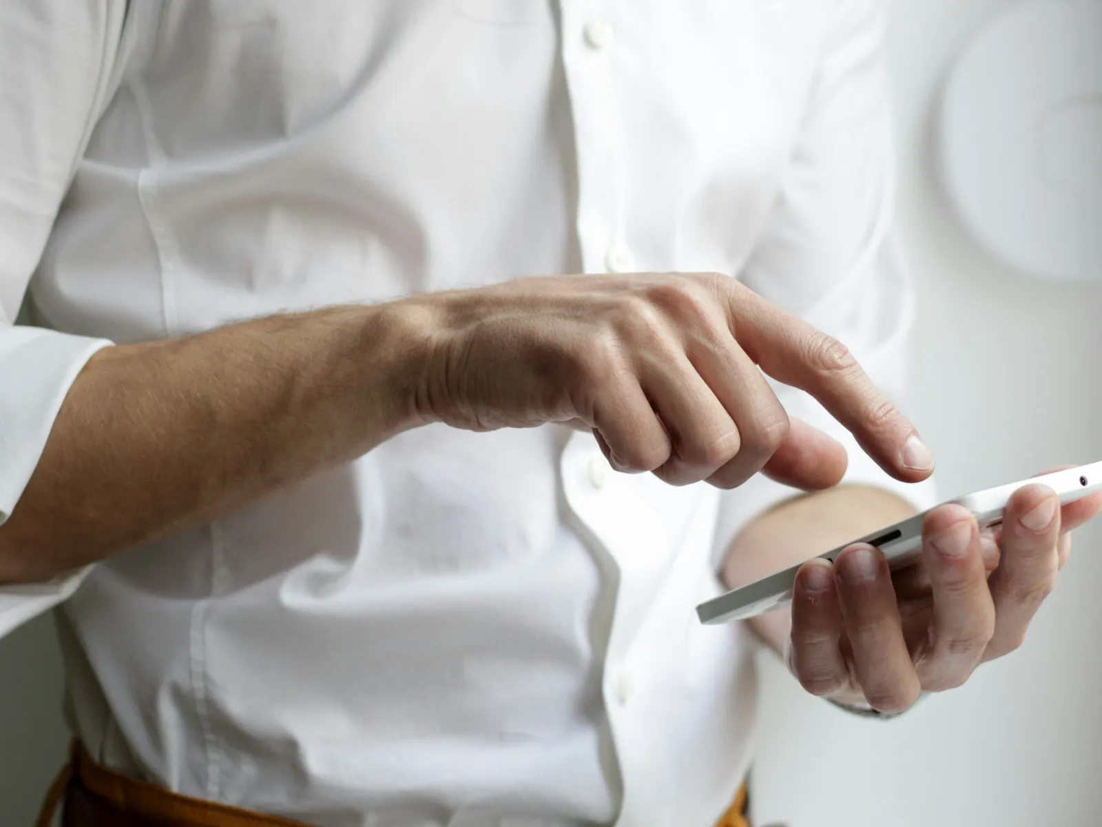 Person wearing white shirt using a white smartphone with one hand tapping the screen with the other.