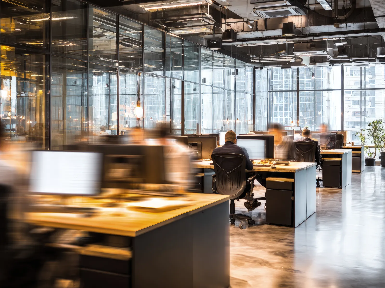 Modern open-plan office with blurred employees working at desks surrounded by glass walls and city views.