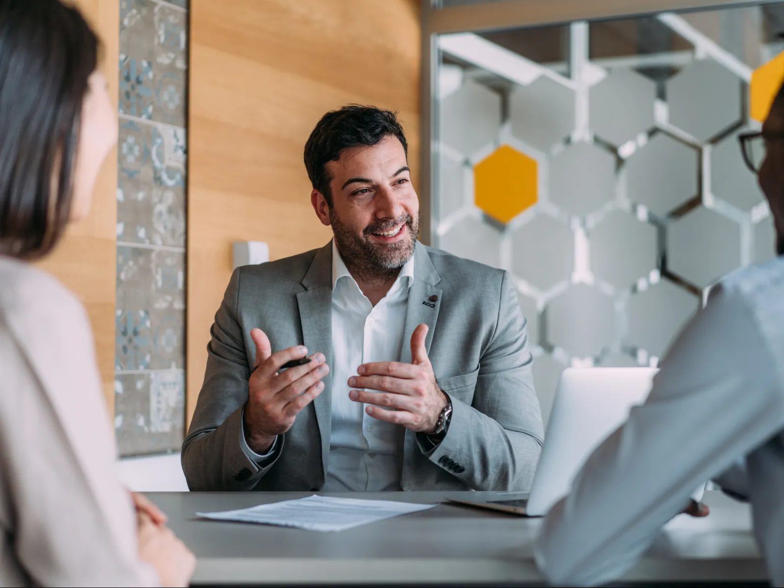 Businessman in a suit explaining with hand gestures during a meeting with two colleagues at a modern office.