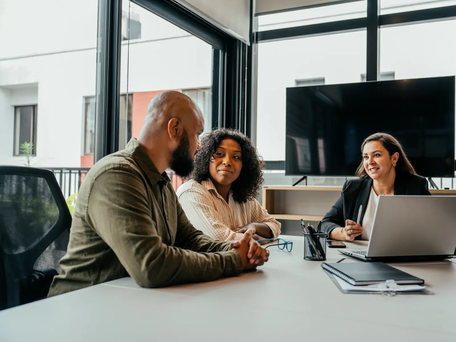 Three diverse business colleagues collaborating on a project using a laptop in a modern office.