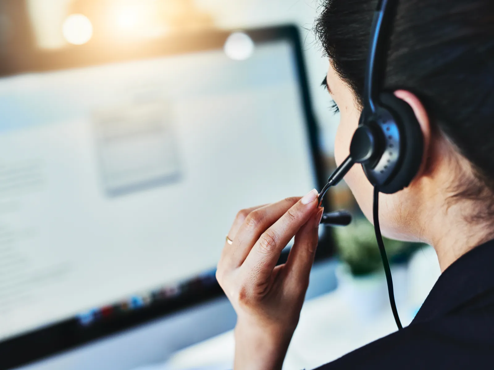 Customer service representative wearing a headset working on a computer in a bright office setting.