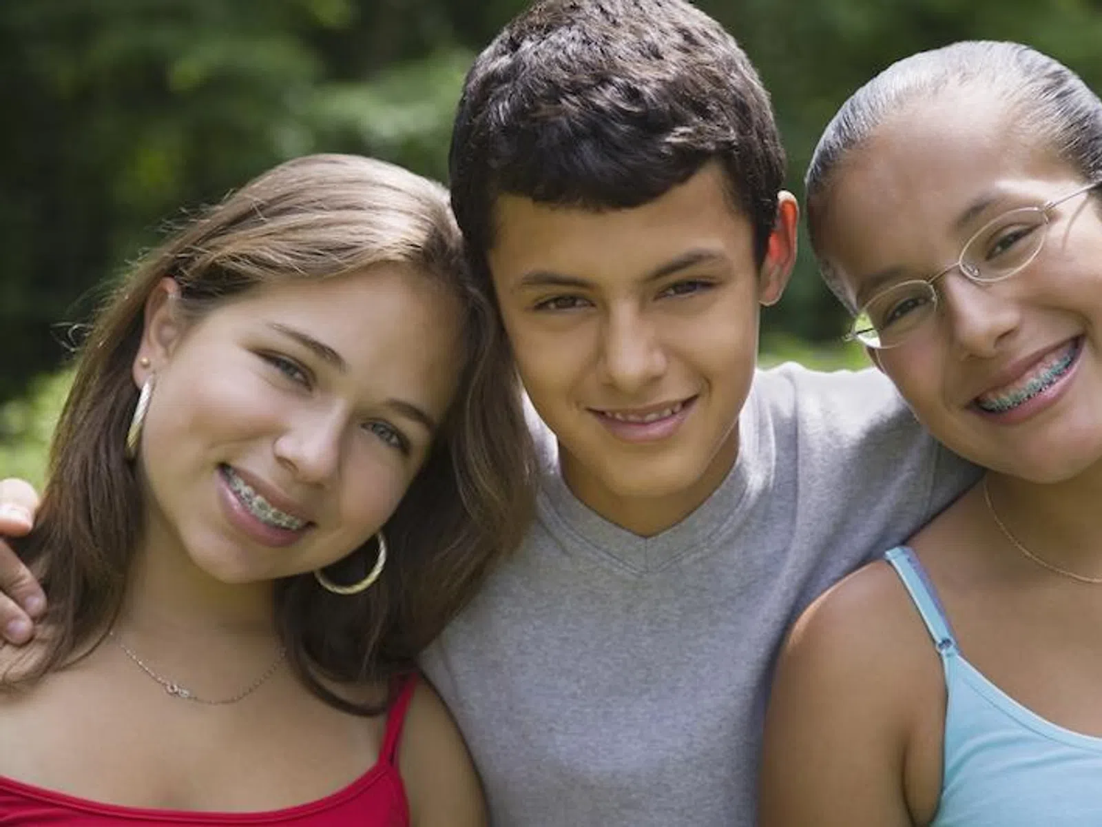 Portrait of three smiling teenagers with braces posing outdoors in casual summer clothes in natural light