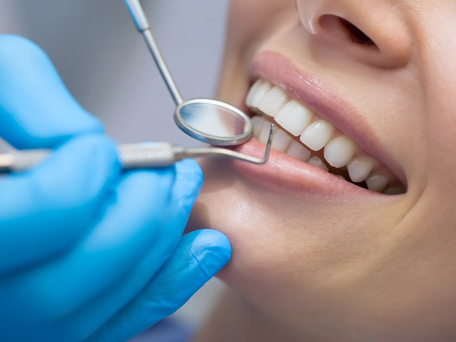 Dentist examining a patient's clean teeth using dental mirror and scaler wearing blue gloves.