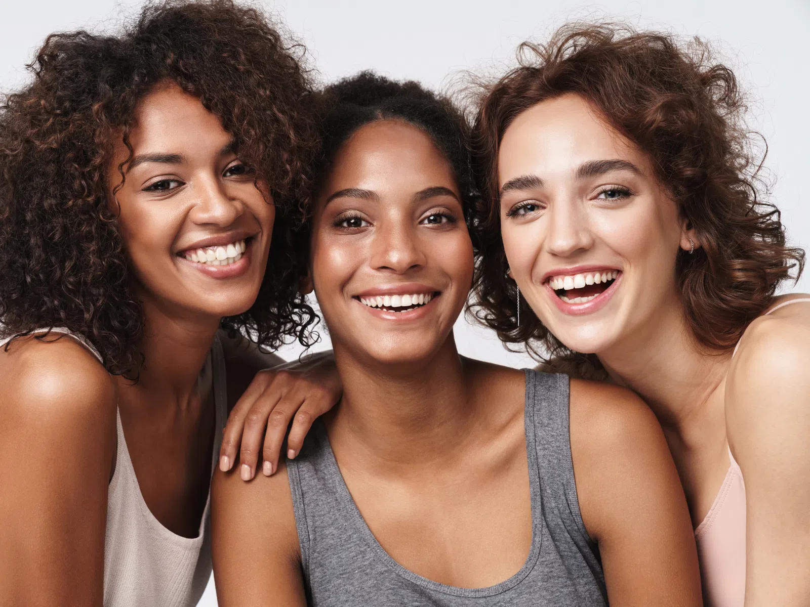Three diverse women smiling together showing friendship and happiness in a close-up portrait.