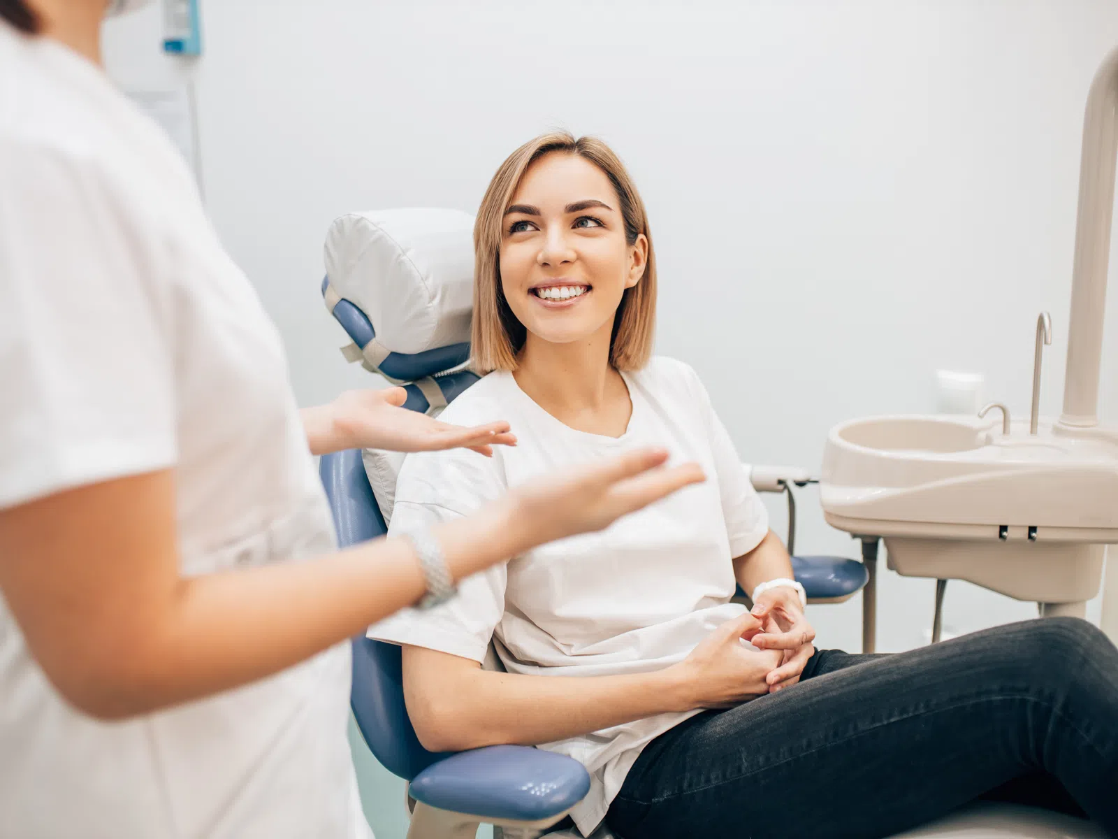 Woman sitting in dental chair smiling and talking to dentist in a modern dental office.