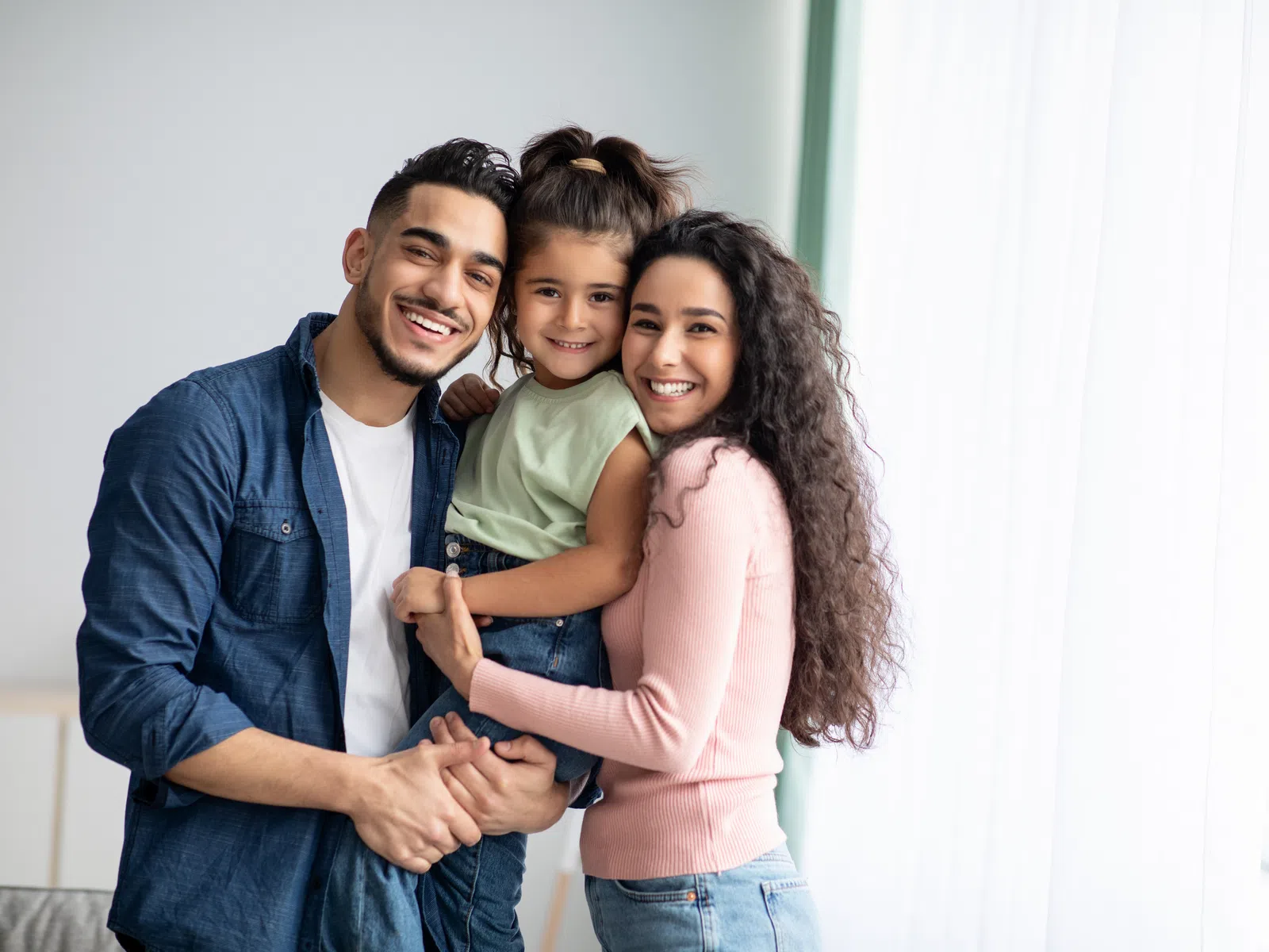 Happy family of three smiling and embracing each other near a bright window in a cozy home setting
