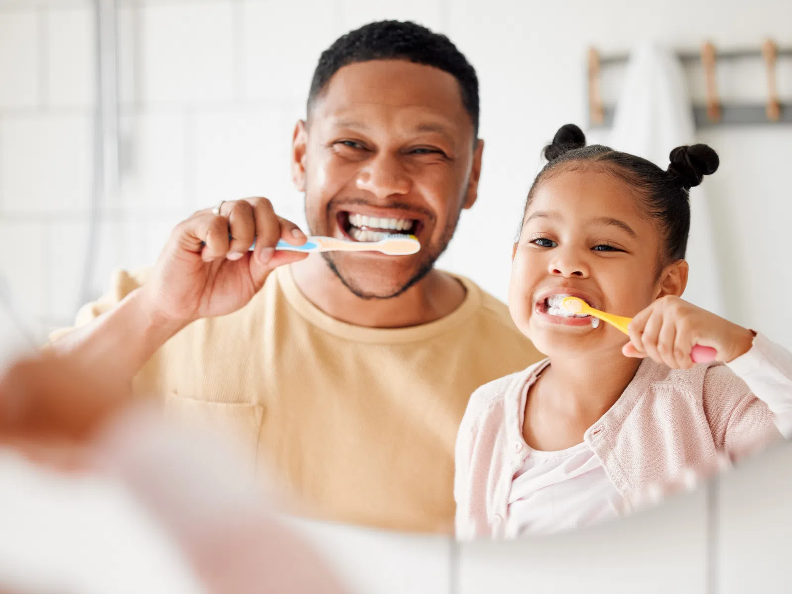 Father and daughter happily brushing their teeth together in a bathroom mirror reflection.