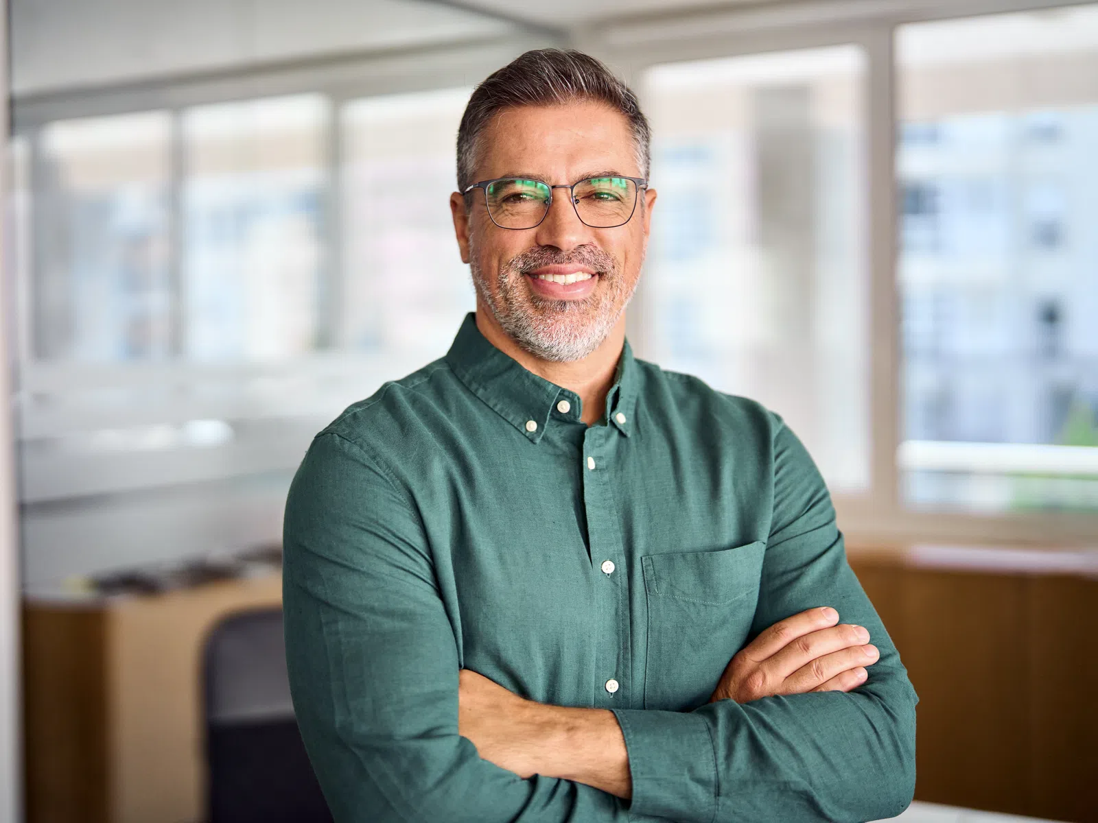 Middle-aged man with glasses smiling confidently with arms crossed in a bright modern office space