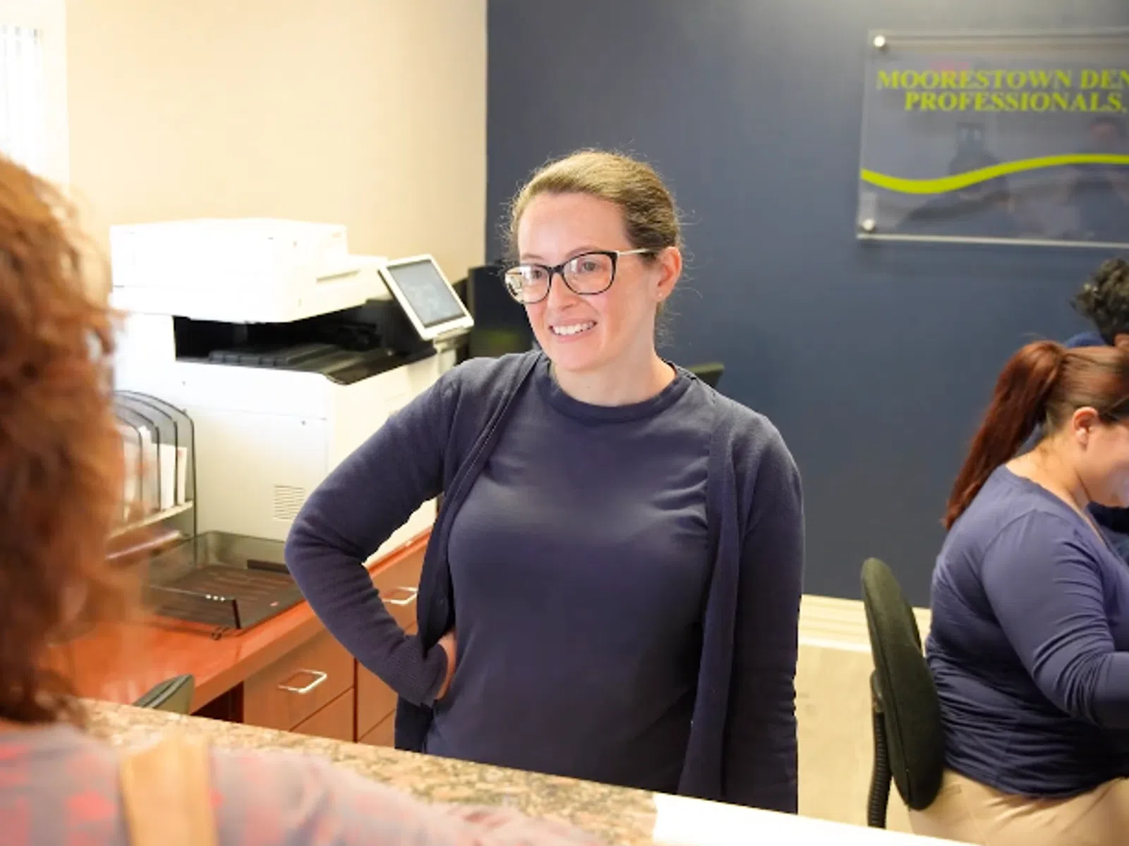 Friendly dental receptionist assisting patient at Moorestown Dental Professionals front desk with staff working in the background
