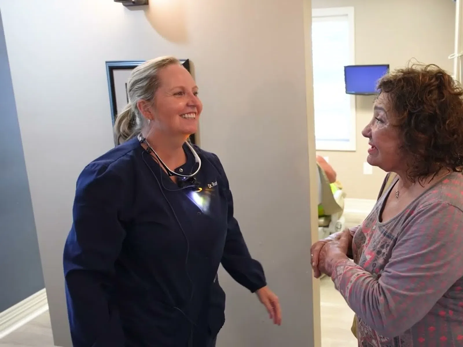 Smiling female dentist talking to a female patient in a bright dental office hallway