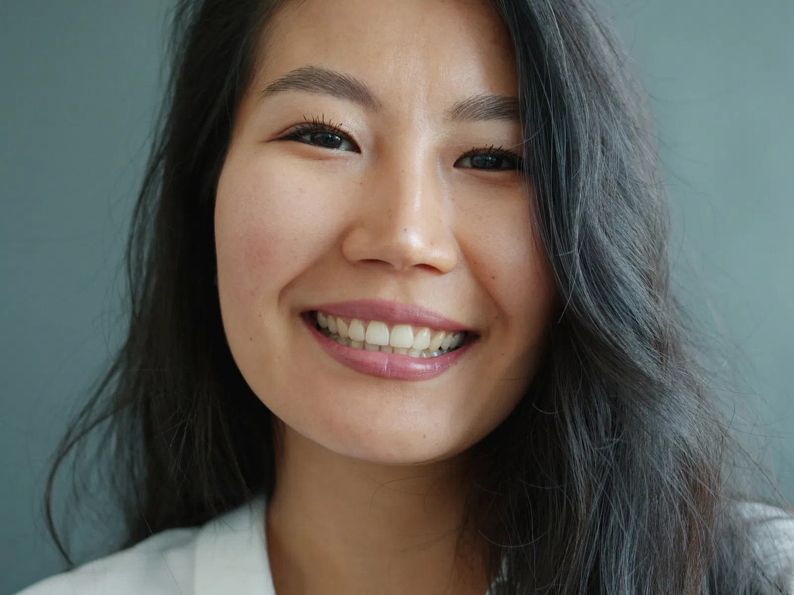 Close-up of a smiling young Asian woman with long dark hair against a gray background