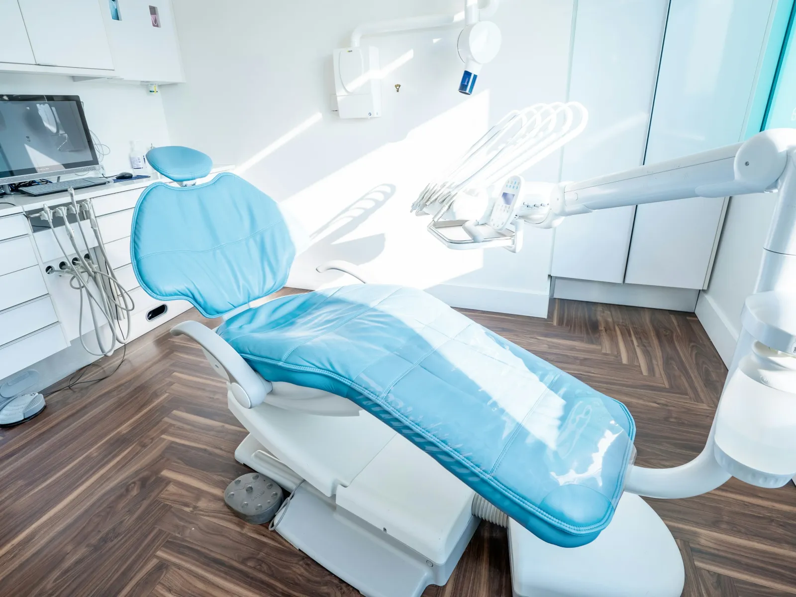 Modern dental clinic with a blue dental chair, equipment, and wooden flooring in a bright room