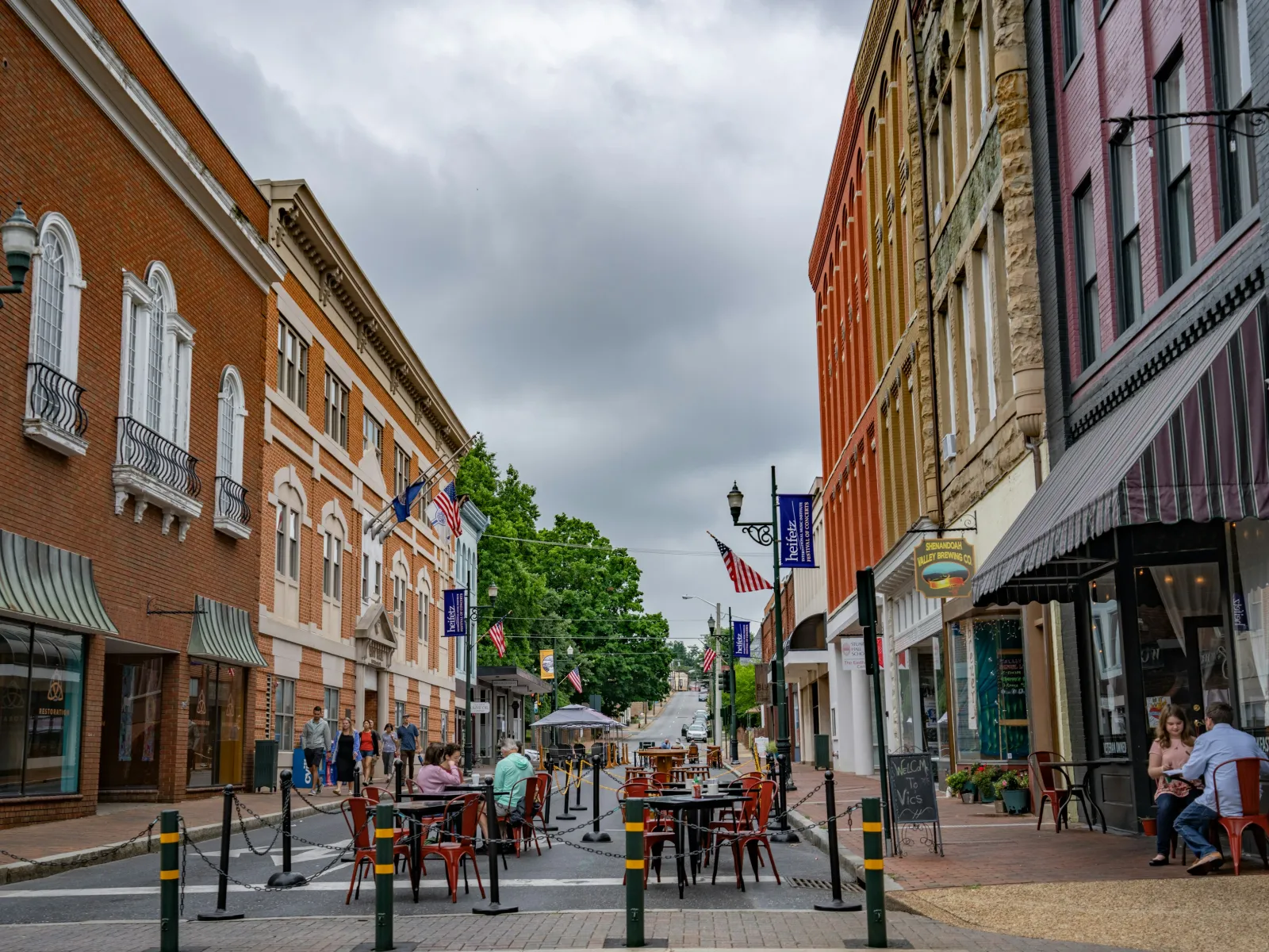 Outdoor dining setup with tables and chairs on a closed street between historic brick buildings under a cloudy sky
