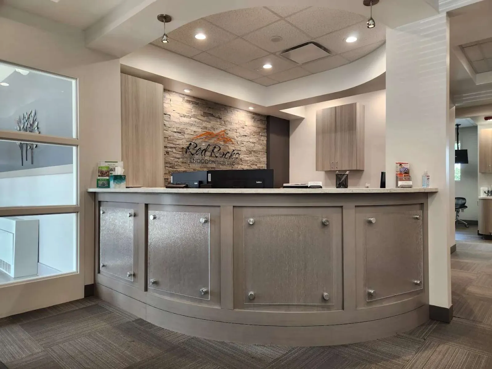 Modern reception area at Red Rocks Endodontics with curved desk, stone accent wall, and soft lighting.
