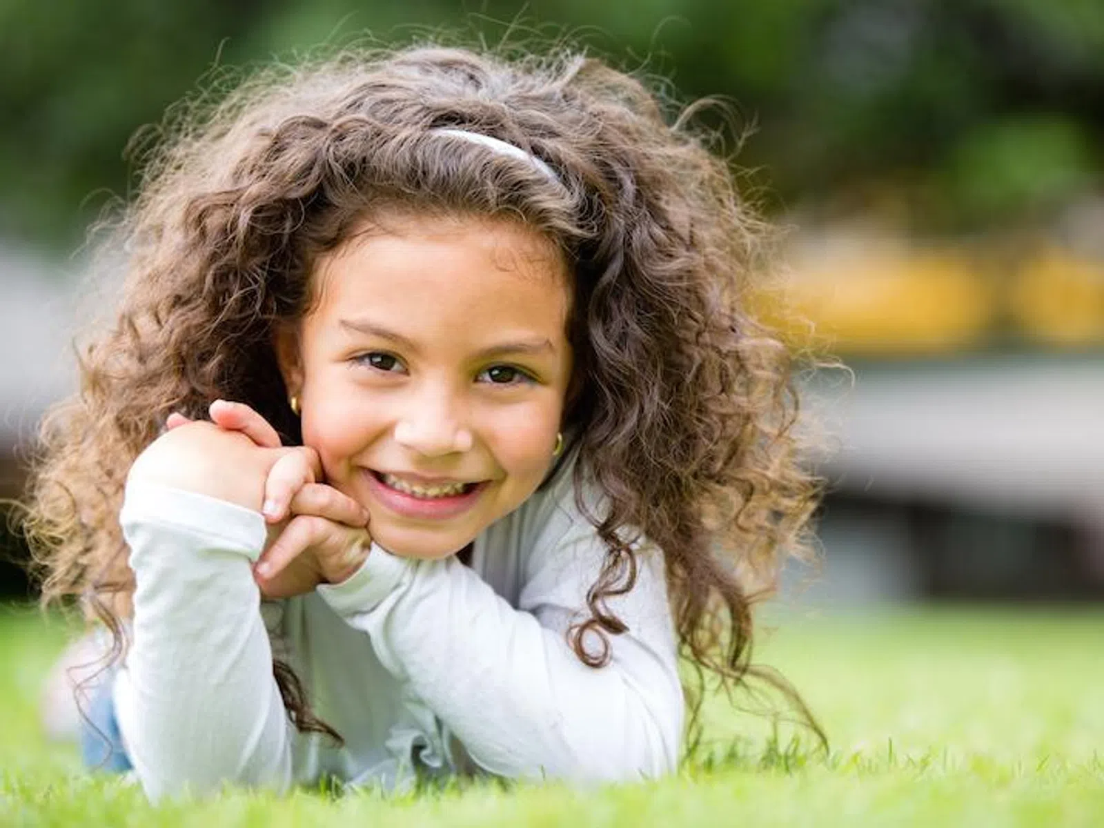 Smiling young girl with curly hair lying on grass outdoors in a sunny park setting