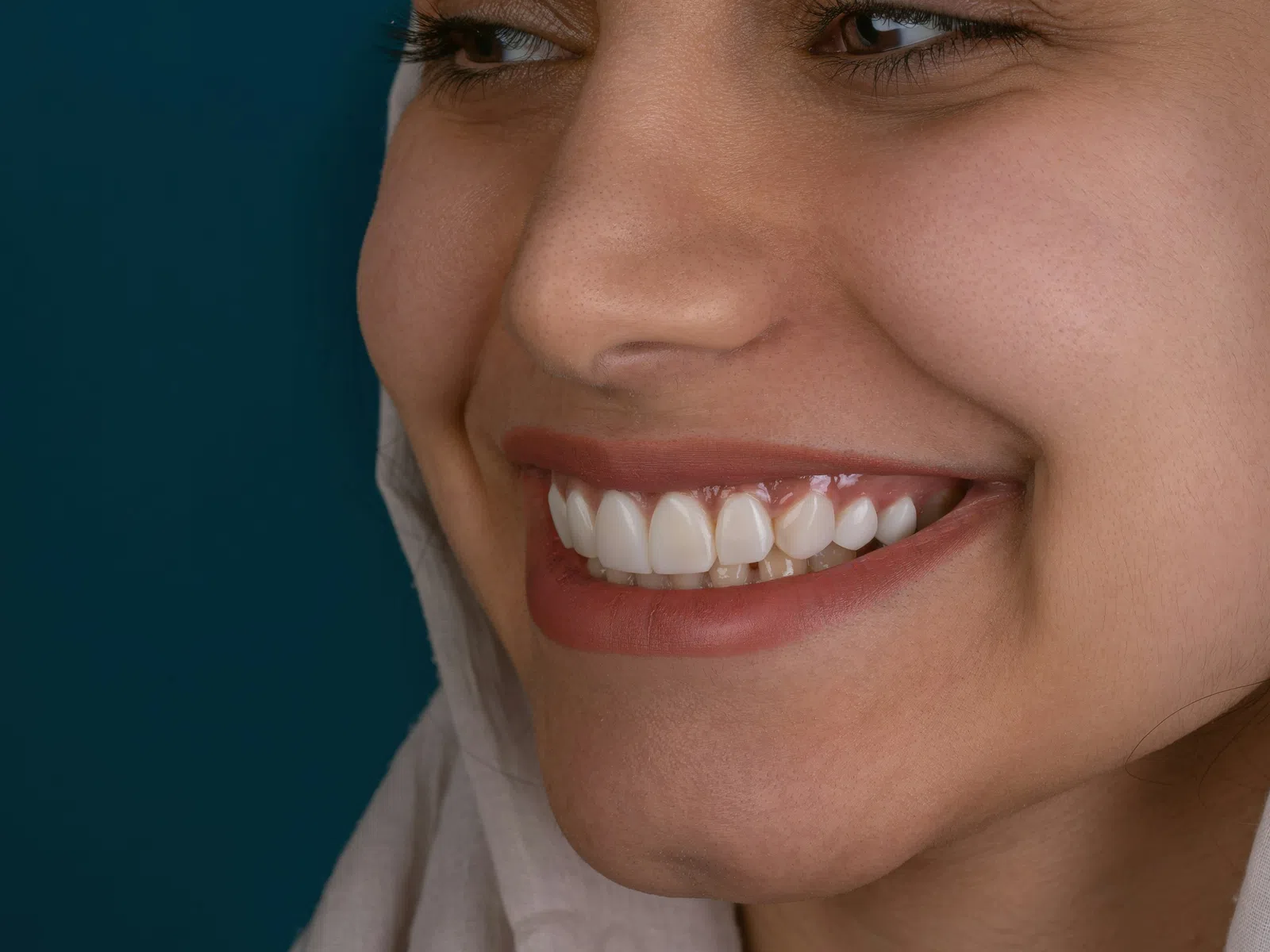 Close-up of a smiling woman with perfect white teeth and natural skin against a dark blue background.