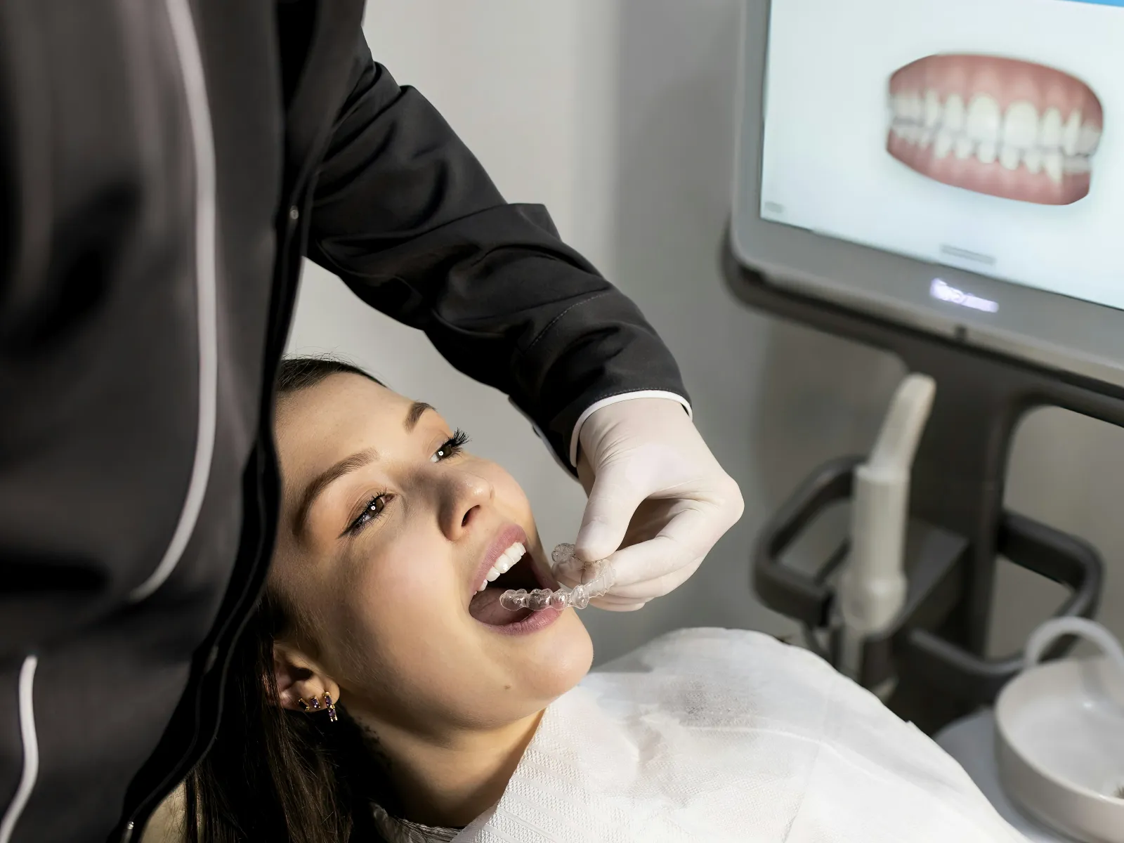 Dentist fitting a clear dental aligner on a young female patient in a modern dental clinic.