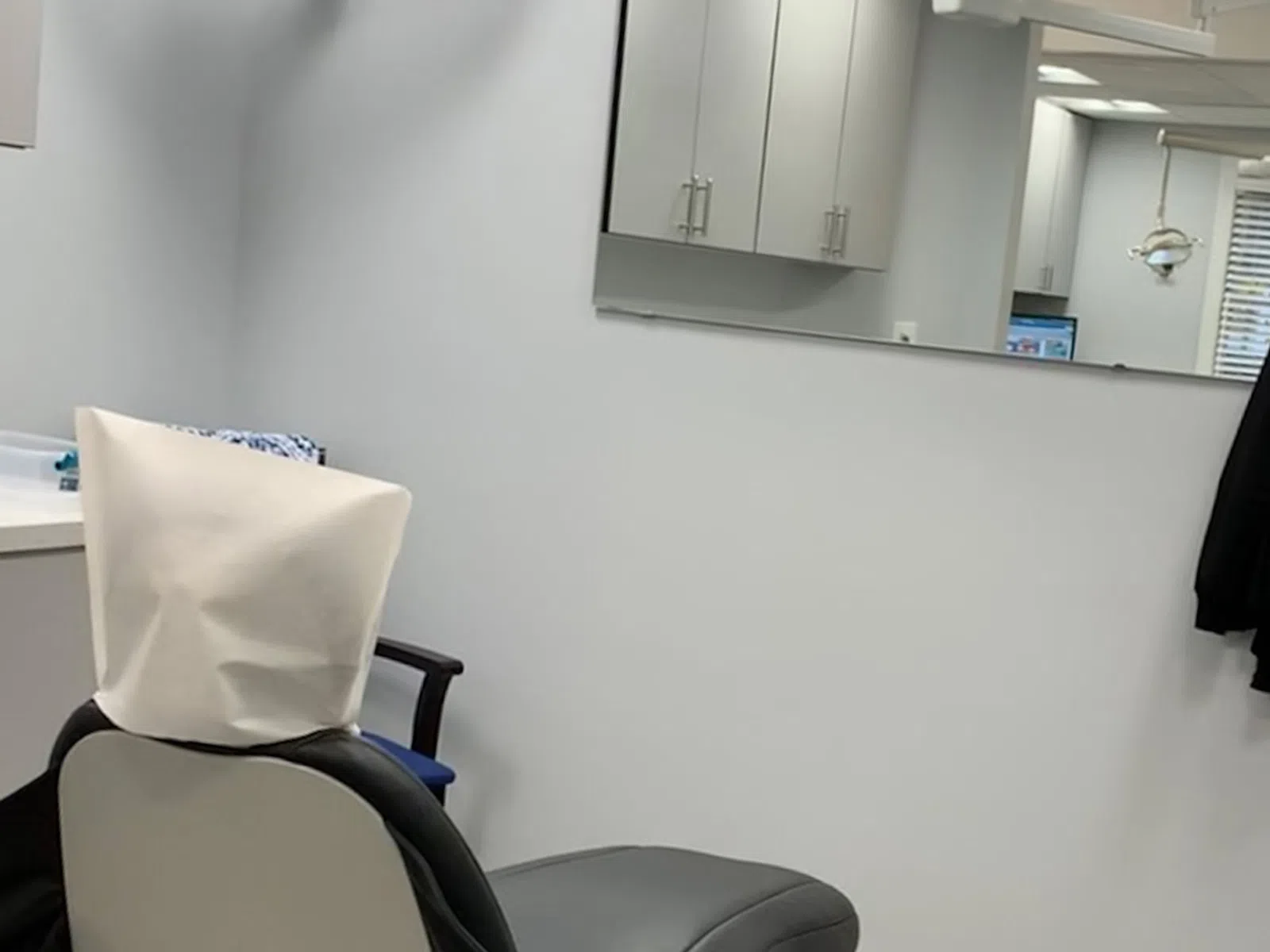 Modern dental office chair with headrest cover, wall-mounted TV, mirror, and cabinetry in clean clinic room.