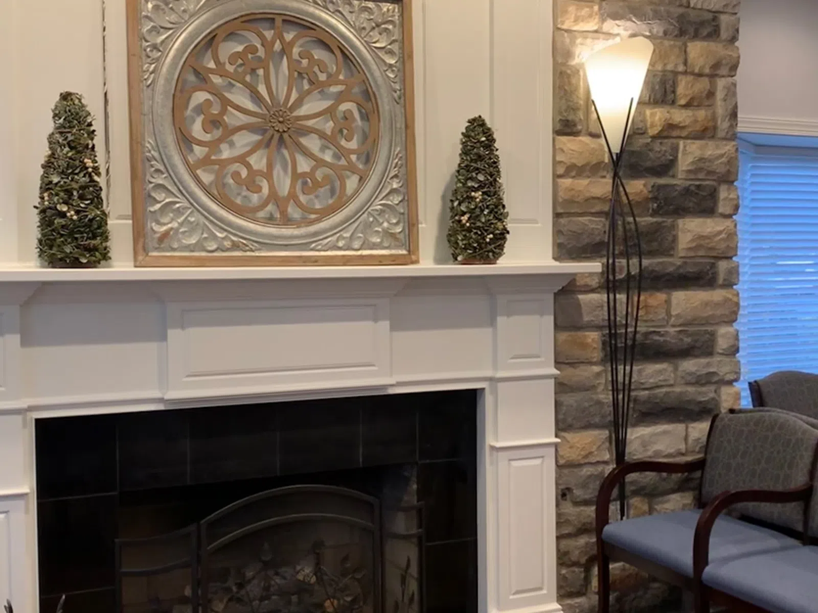 Cozy living room fireplace with decorative metal artwork, topiary trees, stone wall, and floor lamp.