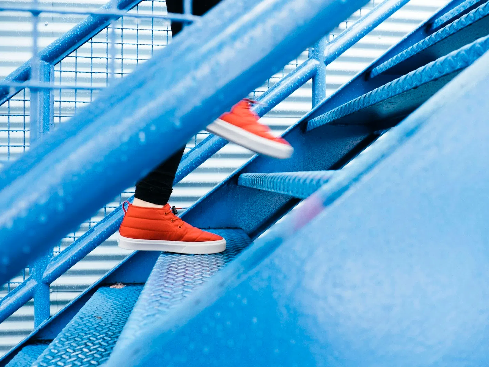 Person wearing bright orange sneakers walking up blue industrial metal stairs outdoors.
