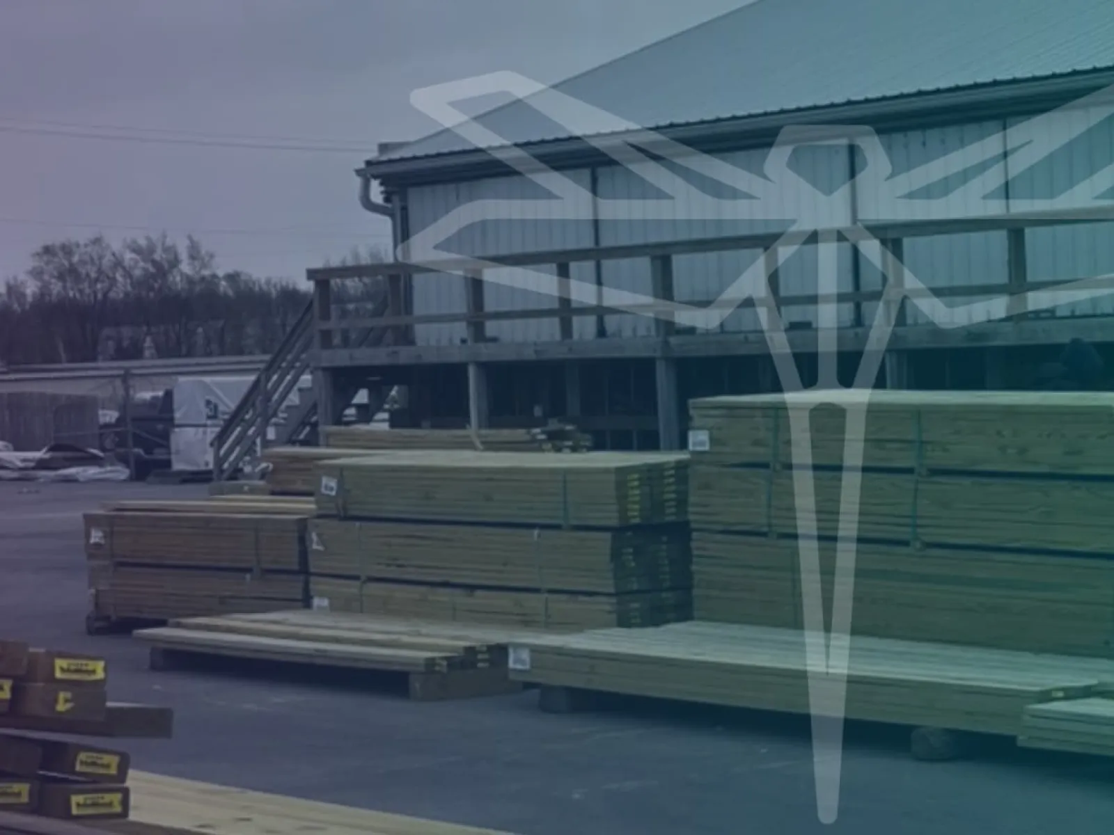 Stacks of lumber and wooden planks outside a warehouse under an overcast sky.