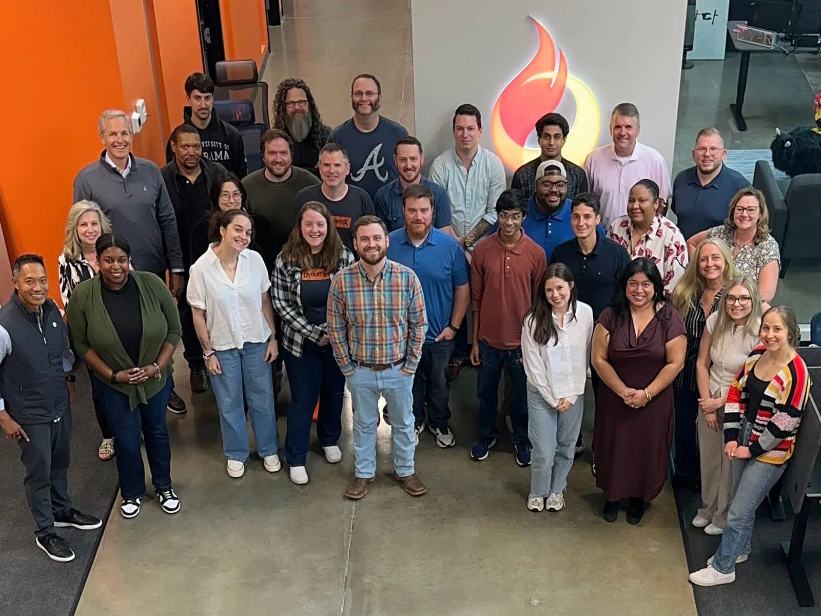 Diverse group of coworkers posing in modern office space with concrete floor and flame logo in background