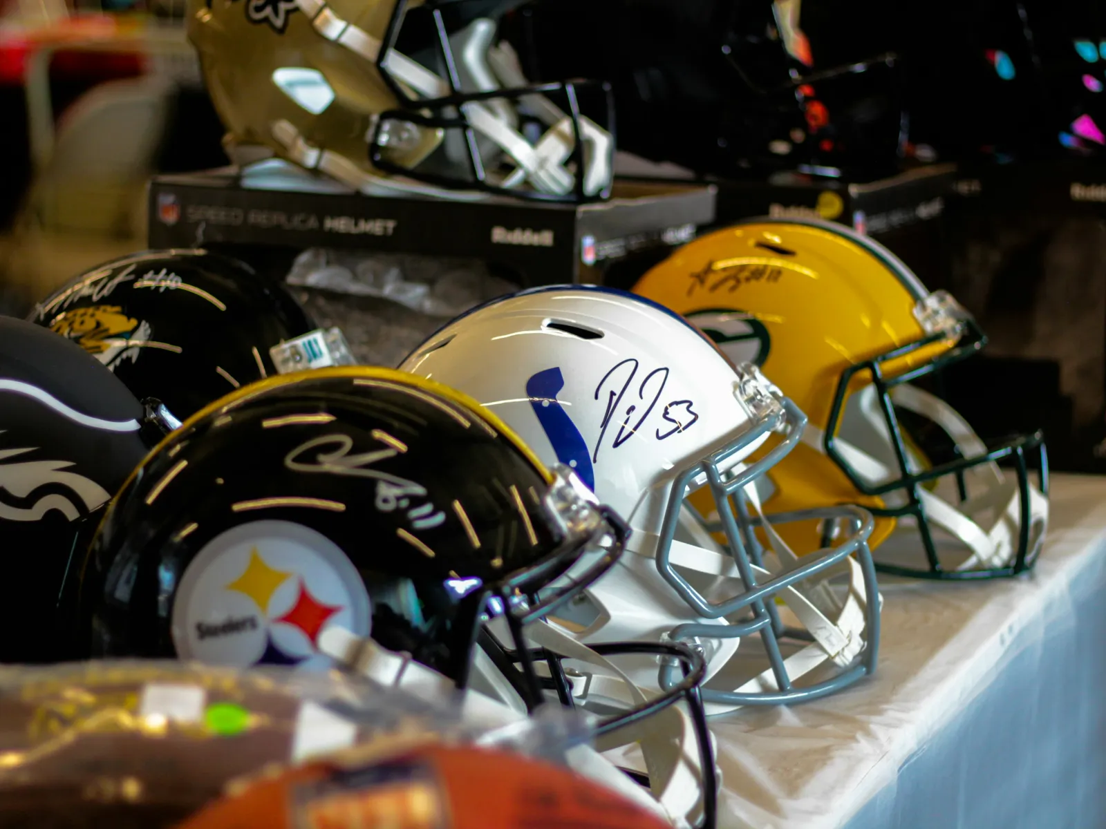 Collection of signed NFL helmets including Steelers, Colts, Packers, Eagles, and Saints displayed on a table.
