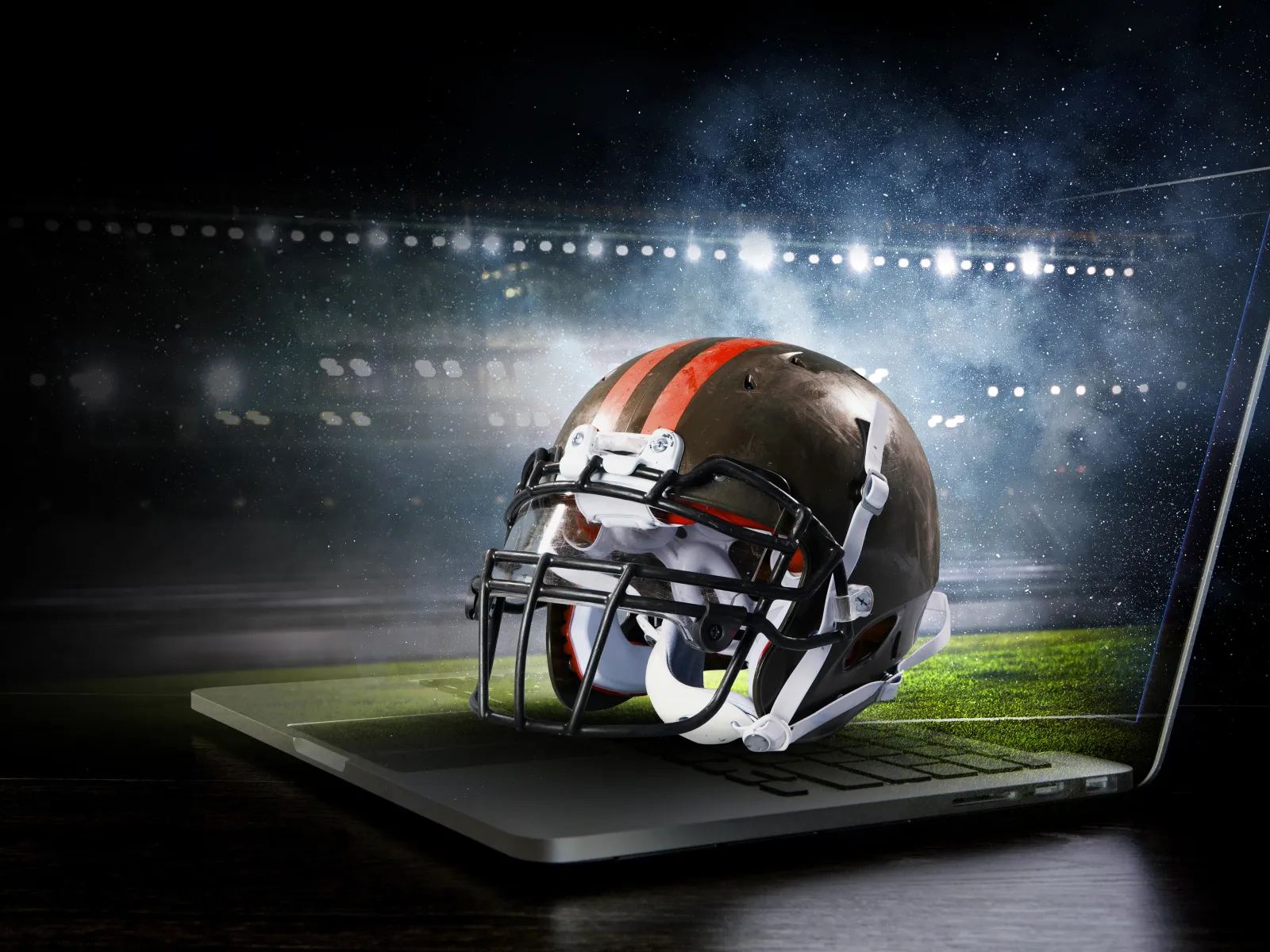 American football helmet emerging from a laptop screen with a stadium background at night