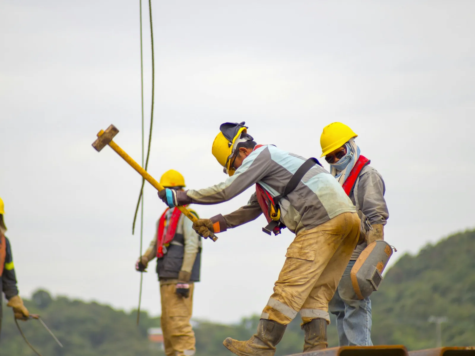 a group of men wearing hardhats and harnesses working on a piece of wood
