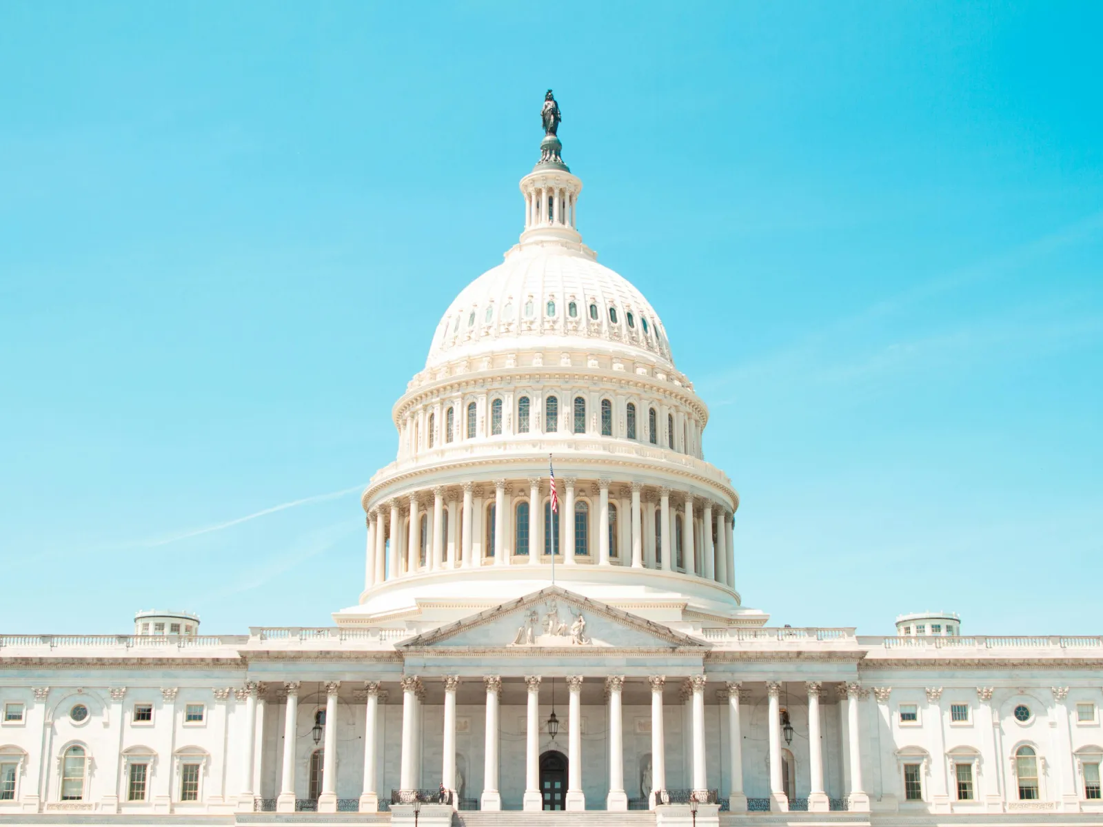 Bright daytime view of the U.S. Capitol building with its iconic white dome and columns against a clear blue sky