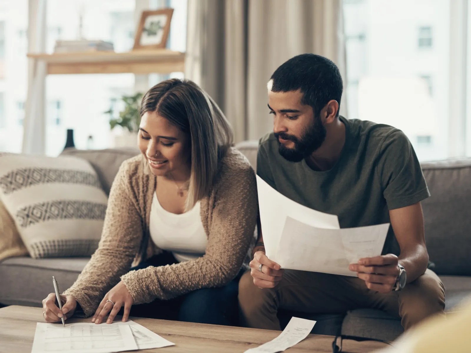 Young couple sitting on sofa reviewing documents and making notes together in a cozy living room.
