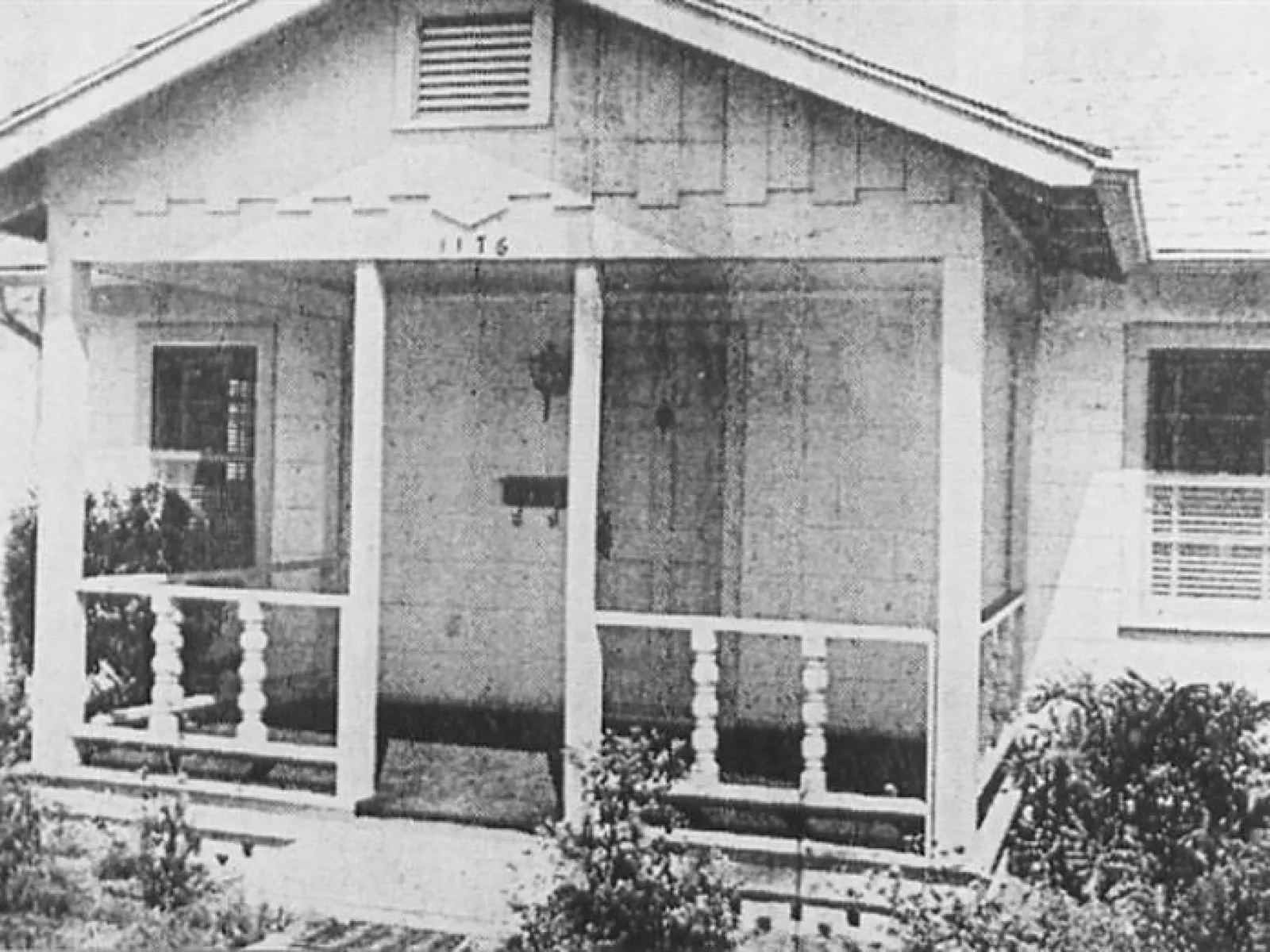 Black and white photo of a small house with a front porch and decorative railings at 1116 address.