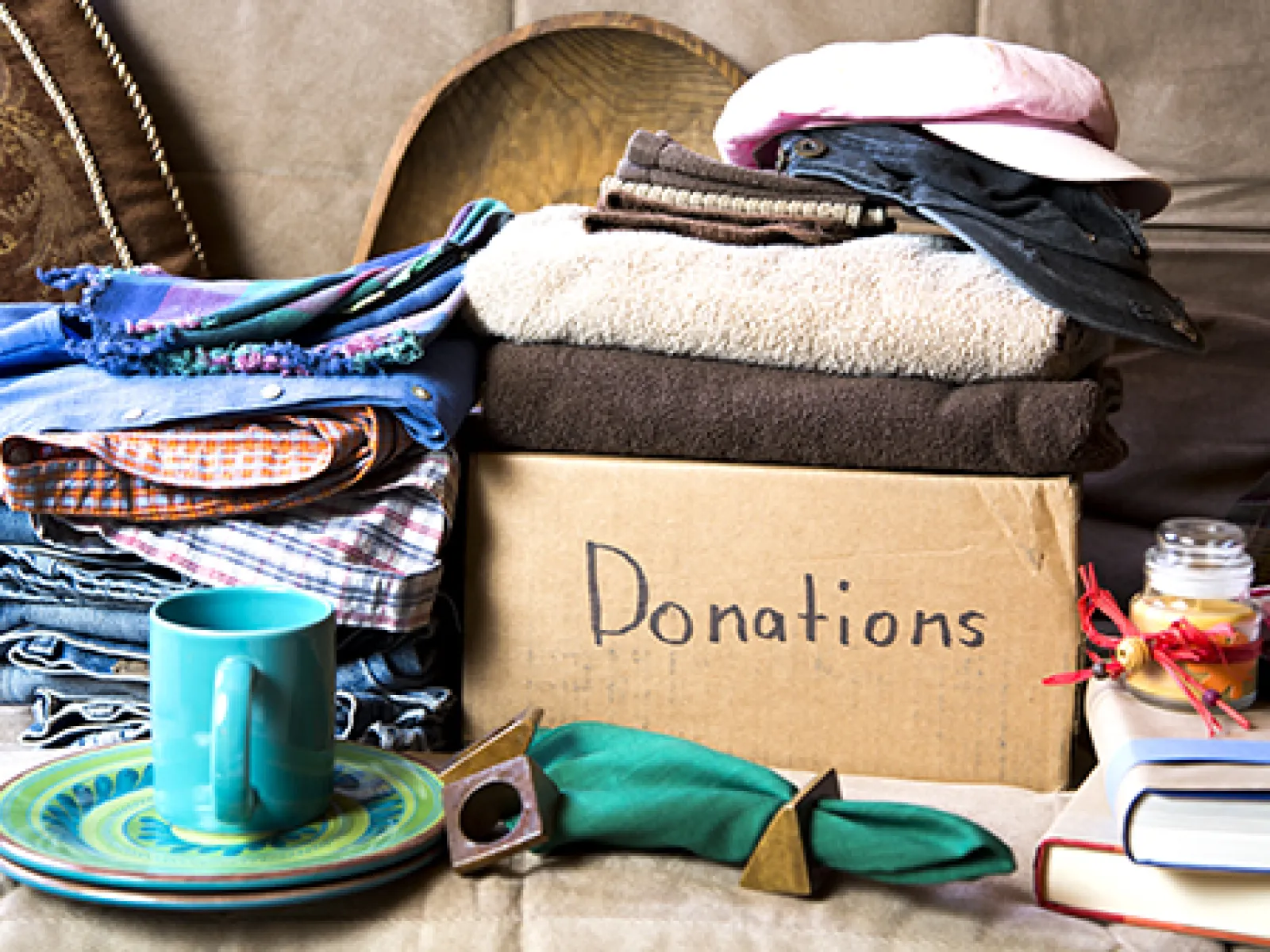 Box labeled donations filled with folded clothes, hats, books, and household items on couch.