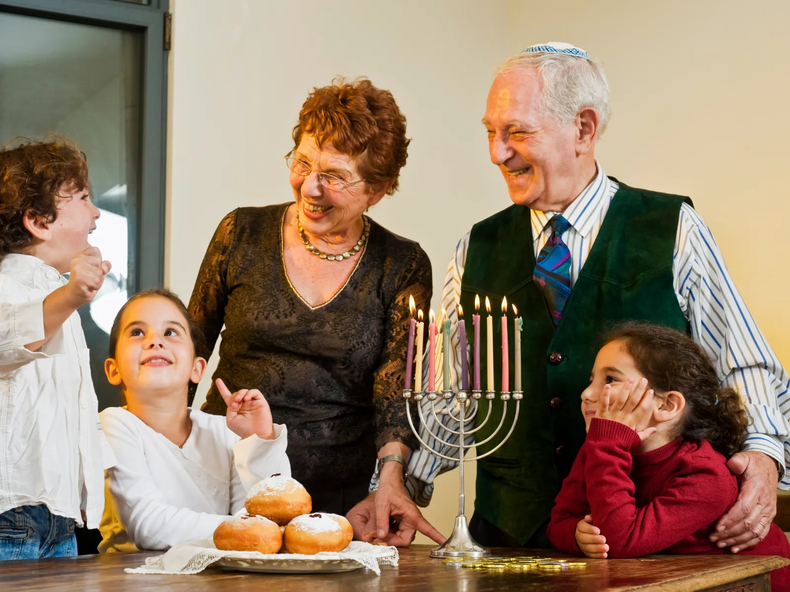 Happy grandparents and grandchildren celebrating Hanukkah with a menorah and traditional jelly donuts at home