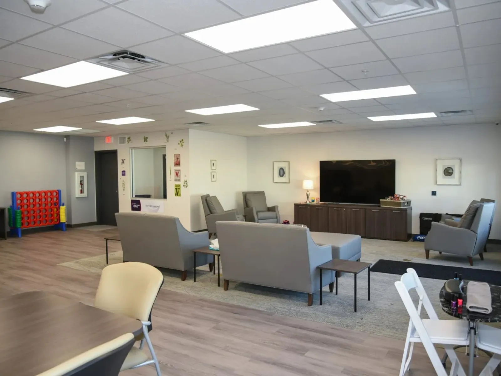 Modern lounge area with gray sofas, armchairs, large TV, and game setup in a bright, spacious room.