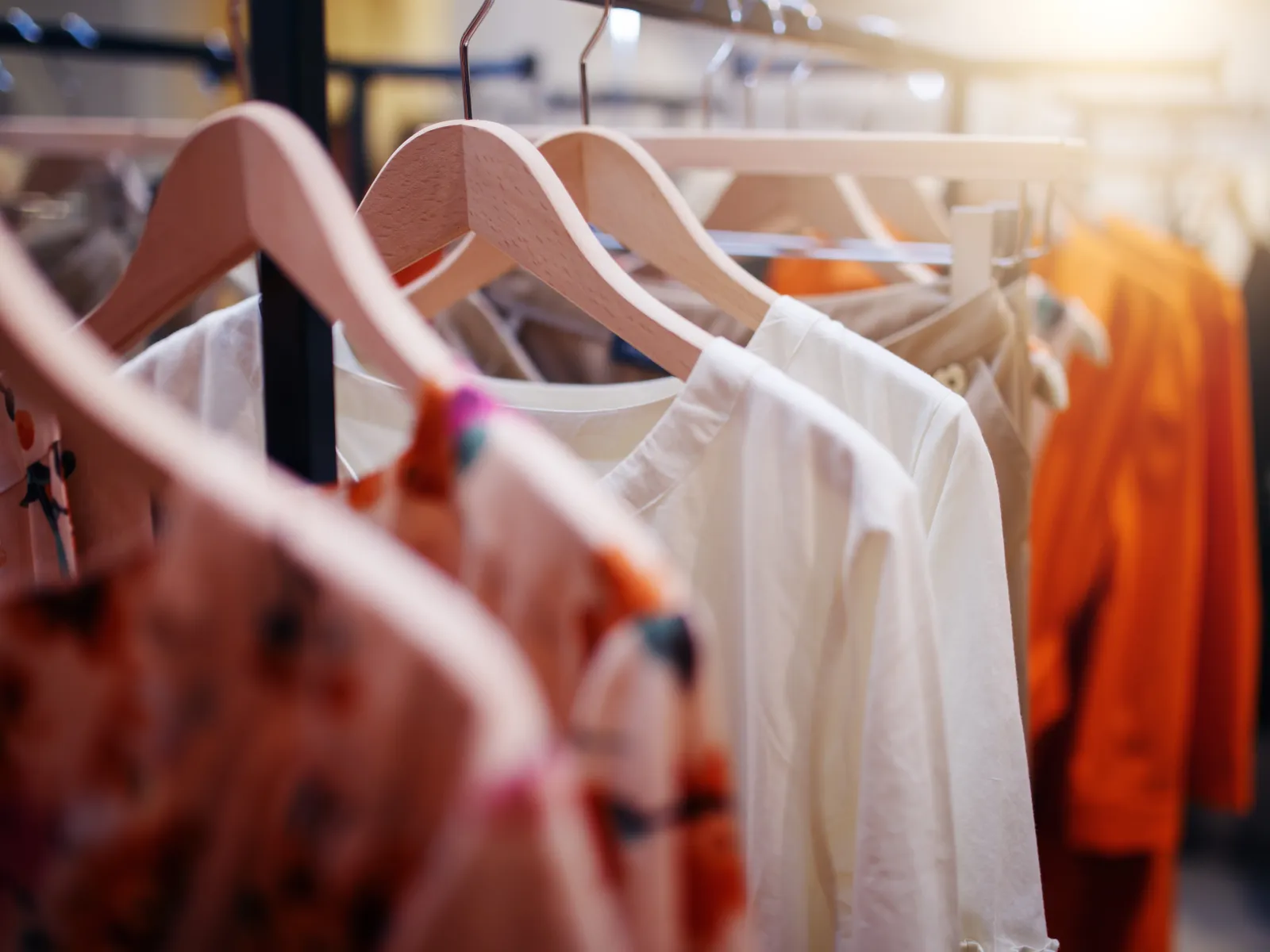 Close-up of colorful and white clothes hanging on wooden hangers in a bright retail store rack.