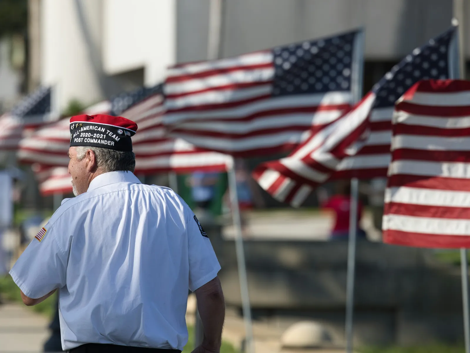 Veteran wearing a cap with American flags lined up in the background on a sunny day outdoors.