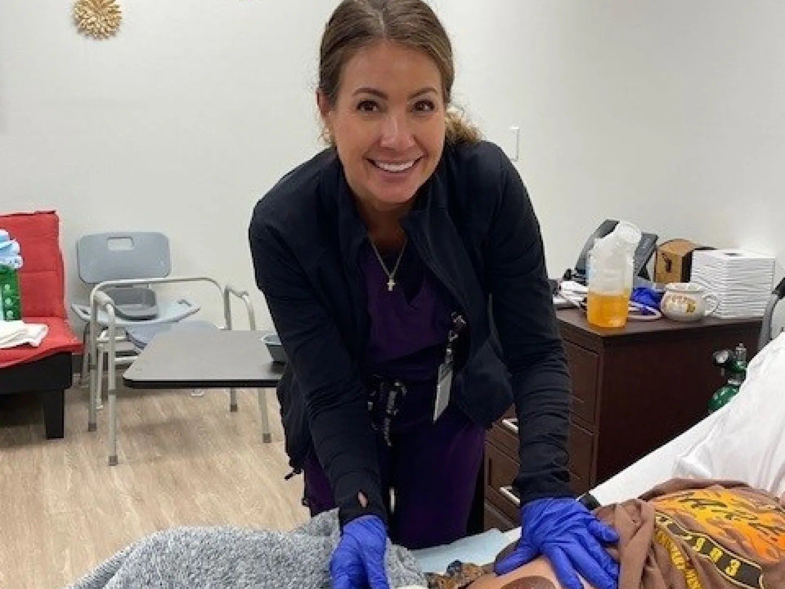 Healthcare professional in purple scrubs applying treatment to patient's abdomen covered with a gray blanket in a clinical setting