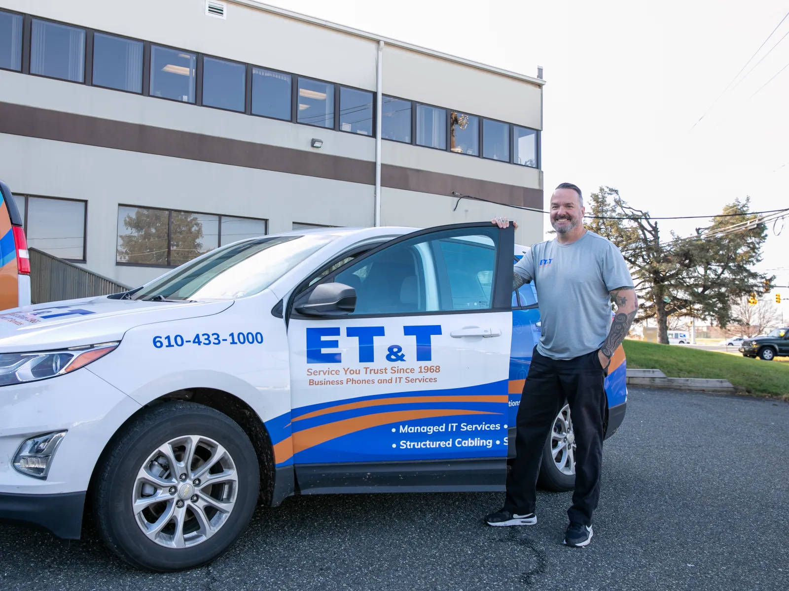 A man stands next to a vehicle branded with ET&T services in front of a building.