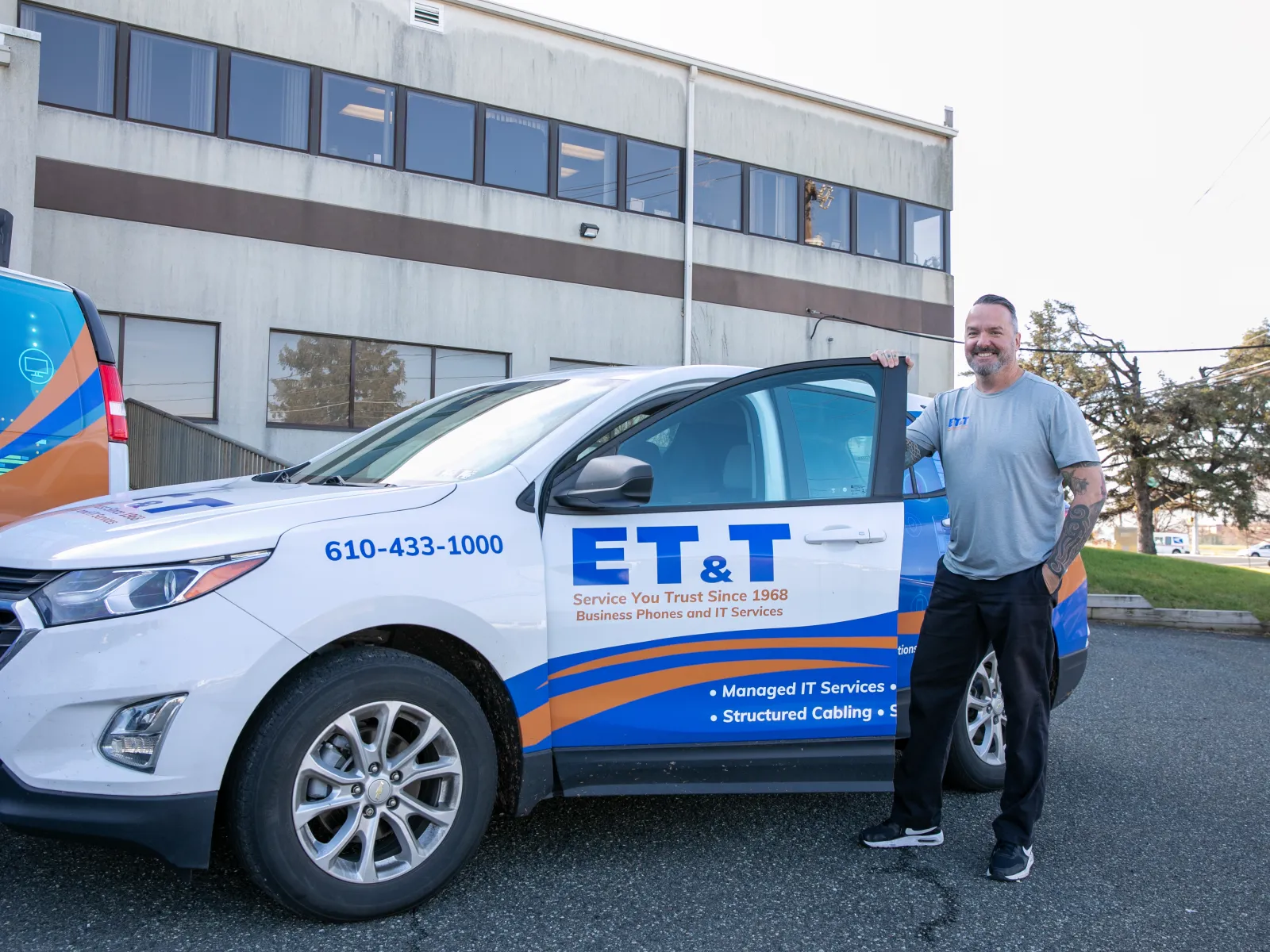 A man stands beside an ET&T branded service vehicle outside an office building.