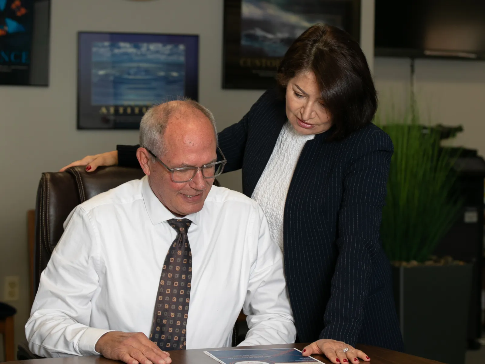 Two colleagues review documents together at a conference table in a professional office setting.