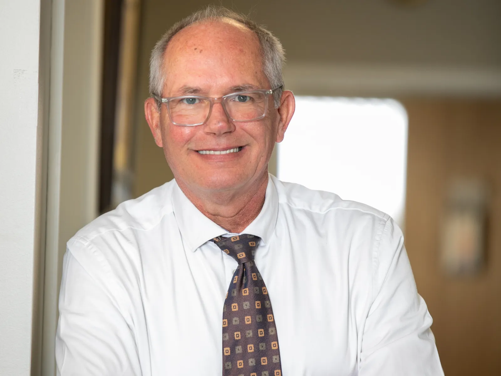 Smiling professional man with glasses, arms crossed, in a well-lit office environment.