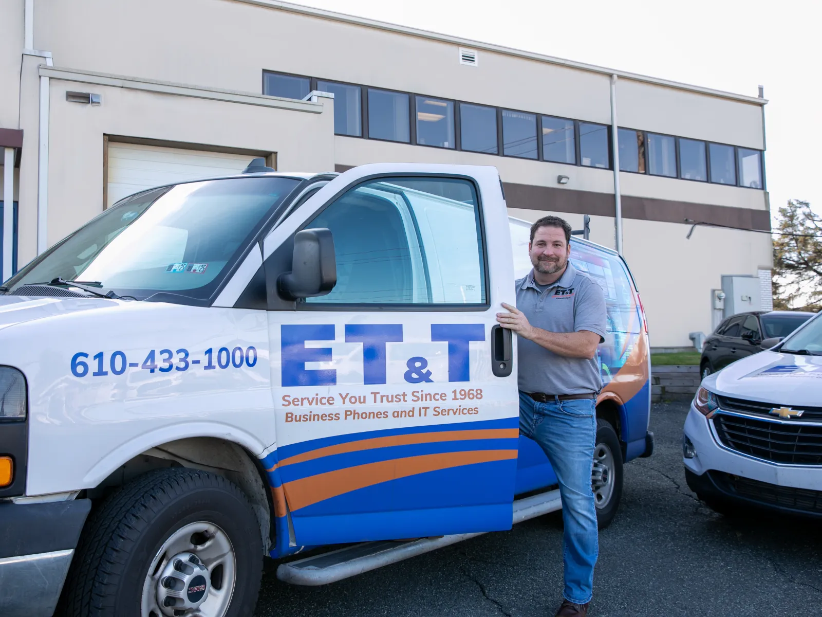 A technician stands by an ET&T service van outside a business building.