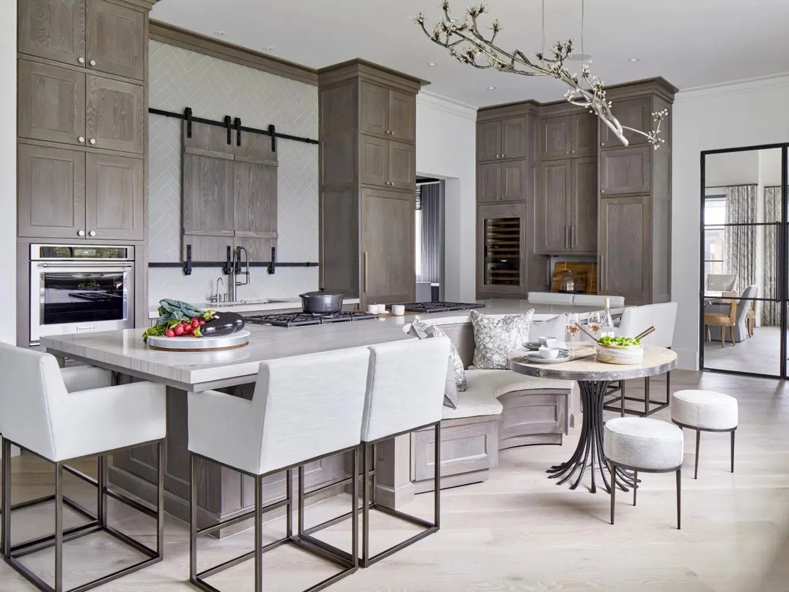 Modern kitchen with gray cabinetry, kitchen island with bar stools, built-in oven, and breakfast nook with round table.
