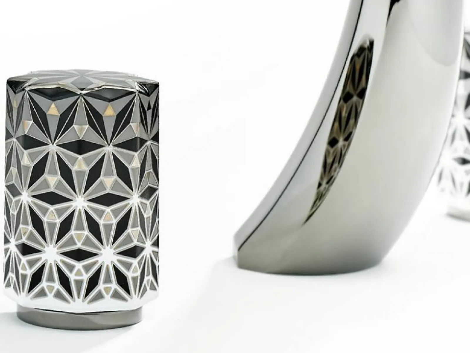 Modern curved chrome faucet with decorative geometric patterned handles on white background