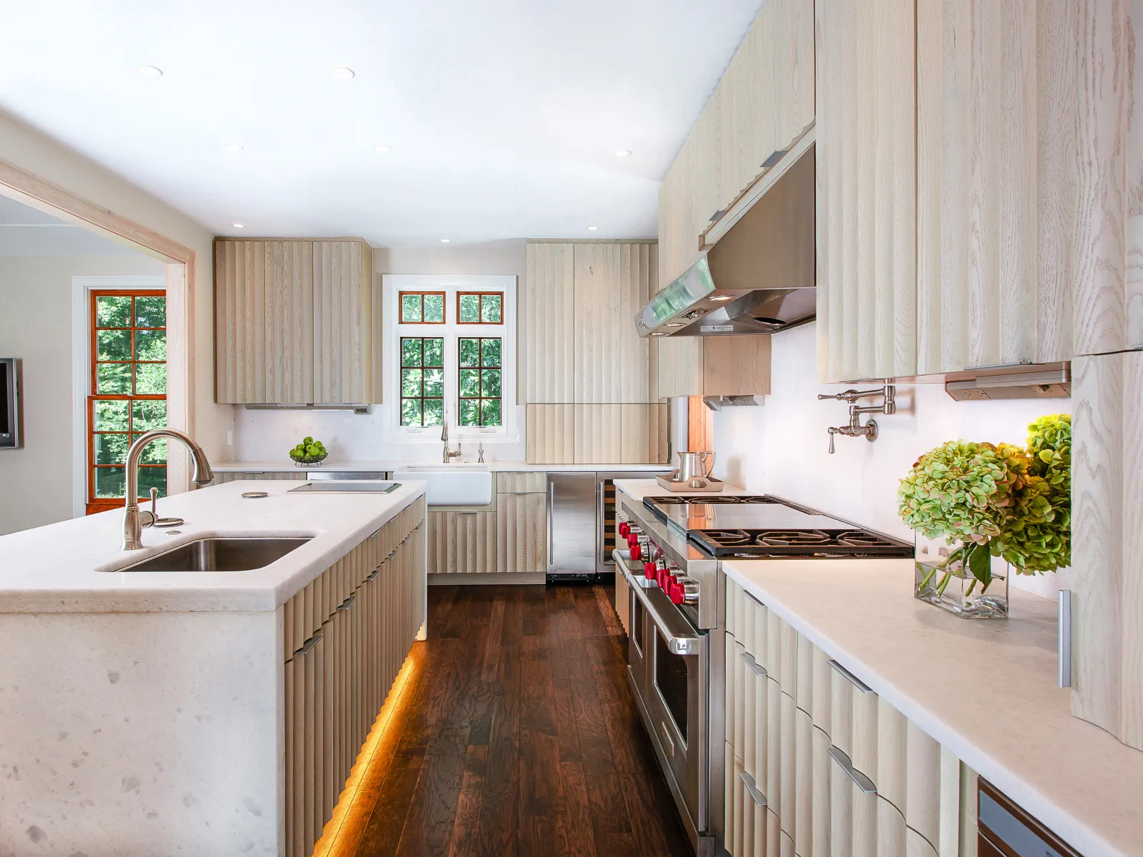 Modern kitchen with light wood cabinets, white countertops, stainless steel appliances, and dark hardwood floors.