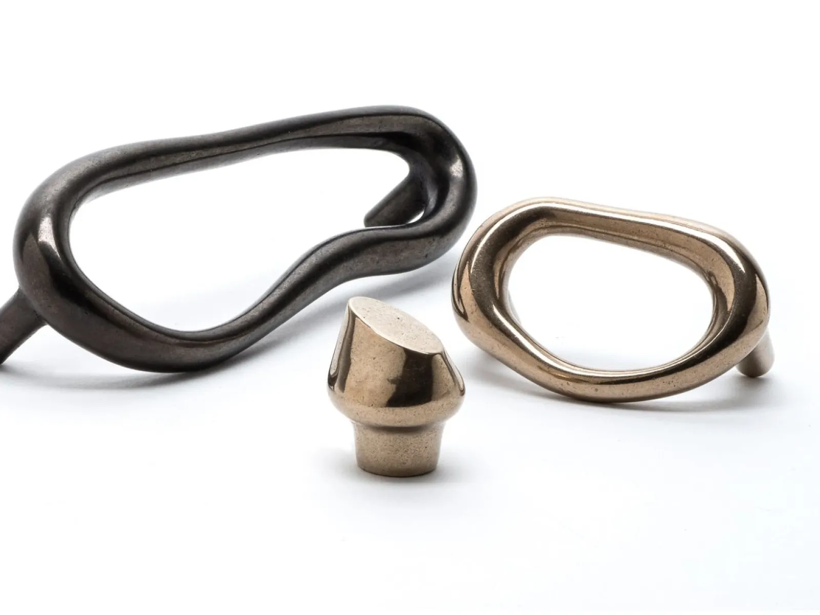 Three stylish metal cabinet handles with organic, irregular shapes in dark and brass finishes on white background.
