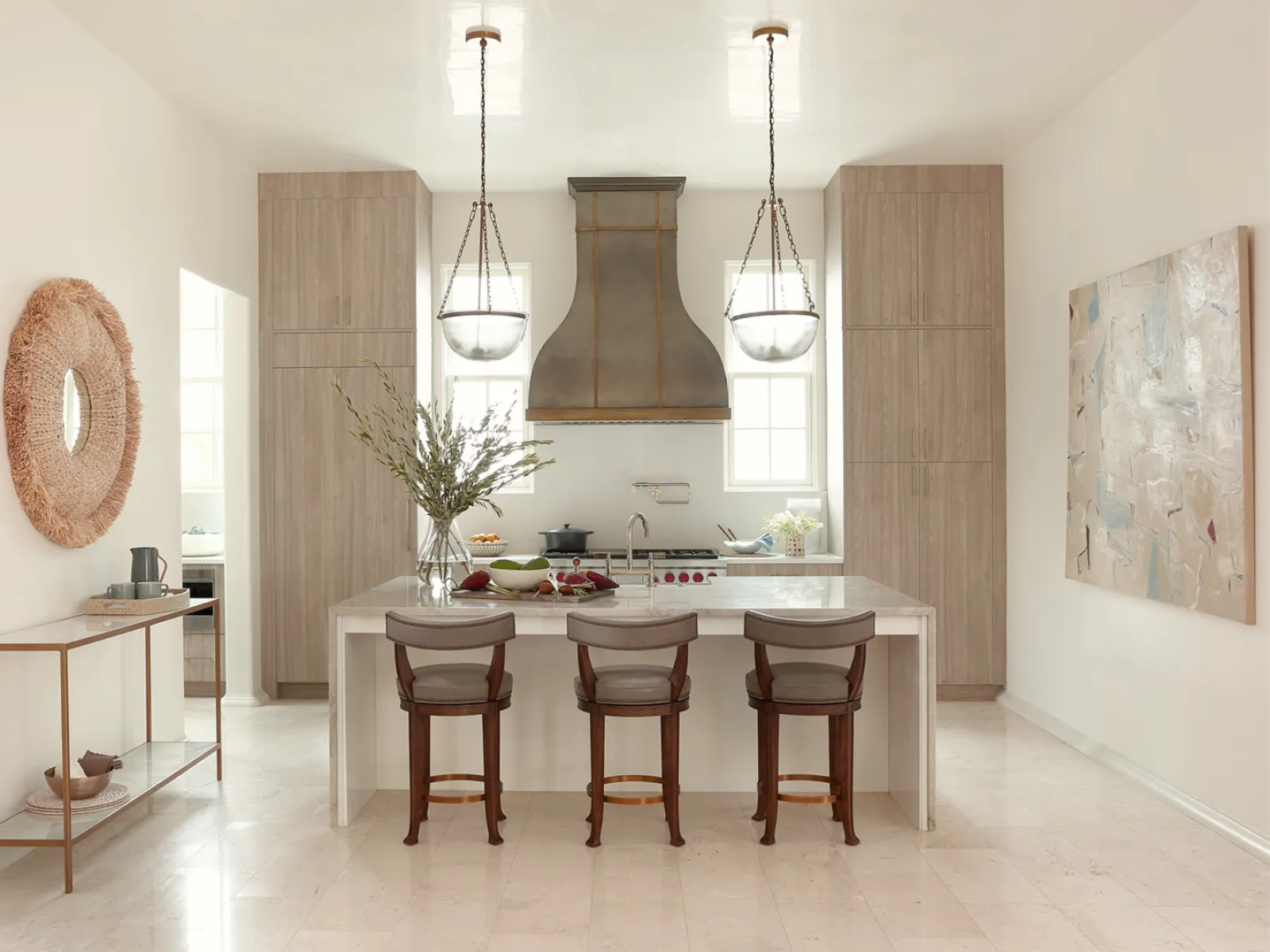 Modern kitchen with wooden cabinetry, marble island, three bar stools, pendant lights, and decorative wall art.
