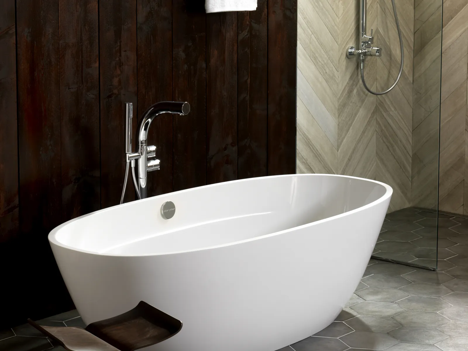 Modern bathroom with white freestanding bathtub, dark wood wall, hexagon floor tiles, and glass shower.