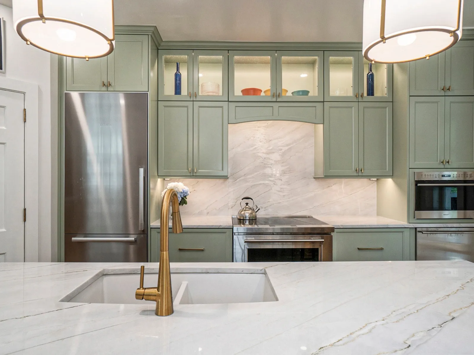 Modern kitchen with light green cabinets, marble countertop, and stylish fixtures for a sleek design.